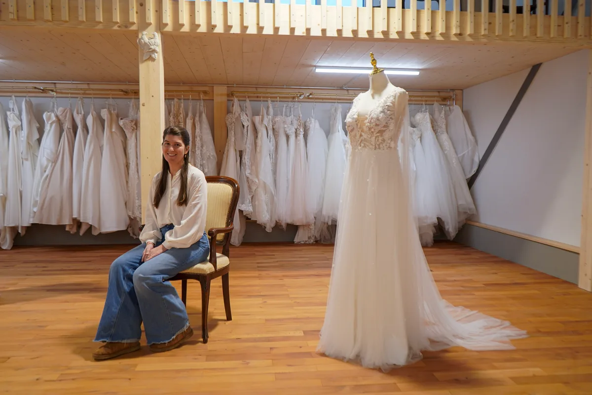 Man sieht eine Frau vor Hochzeitskleidern.